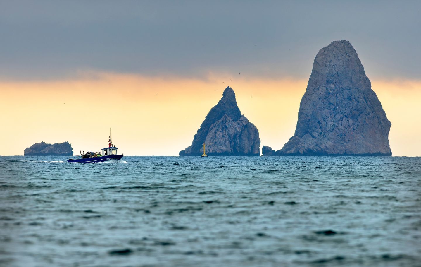 Una barca de pesca artesanal navega davant dels Tascons Petits i els Tascons Grossos, que fan companyia al Carall Bernat, a la dreta